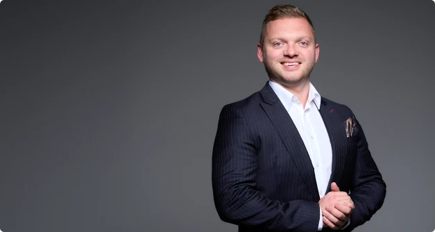  W lewym górnym rogu znajduje się zdjęcie mężczyzny w eleganckim garniturze, z uśmiechem, stojącego na tle ciemnego tła. Jest to zdjęcie biznesowe