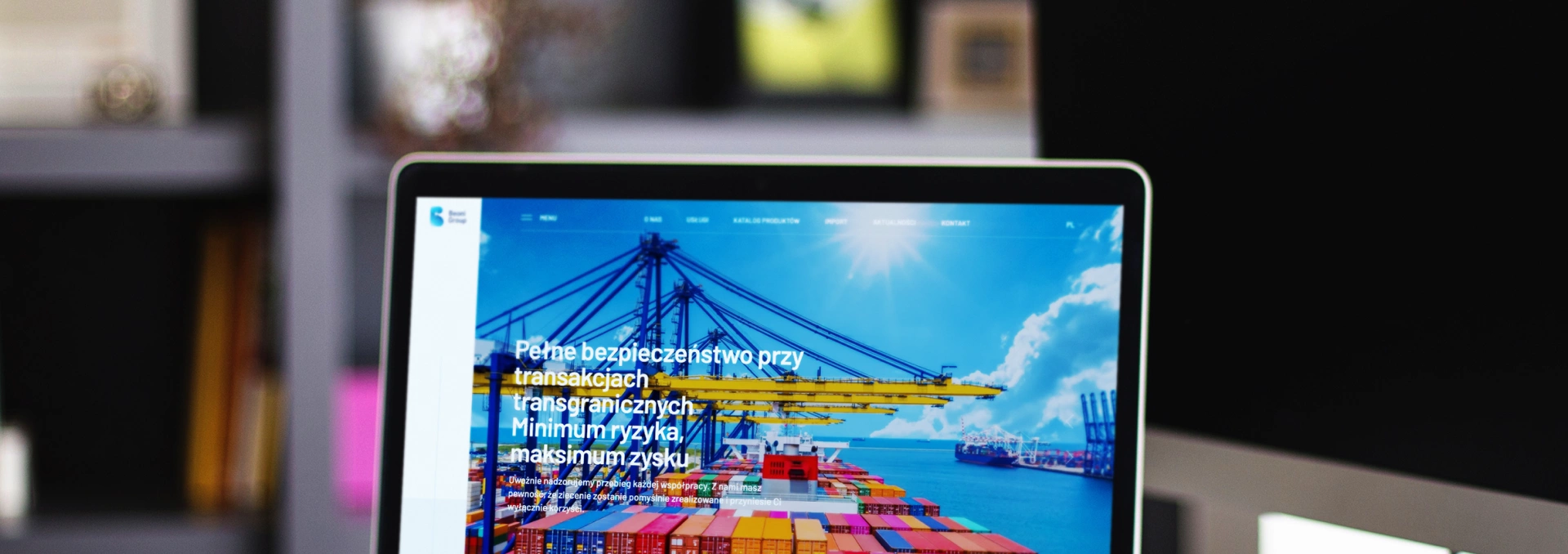 Ekran laptopa pokazuje stronę Beoni Group, firmę zajmującą się handlem i logistyką. Grafika portu podkreśla import i eksport, a strona akcentuje bezpieczeństwo transakcji.